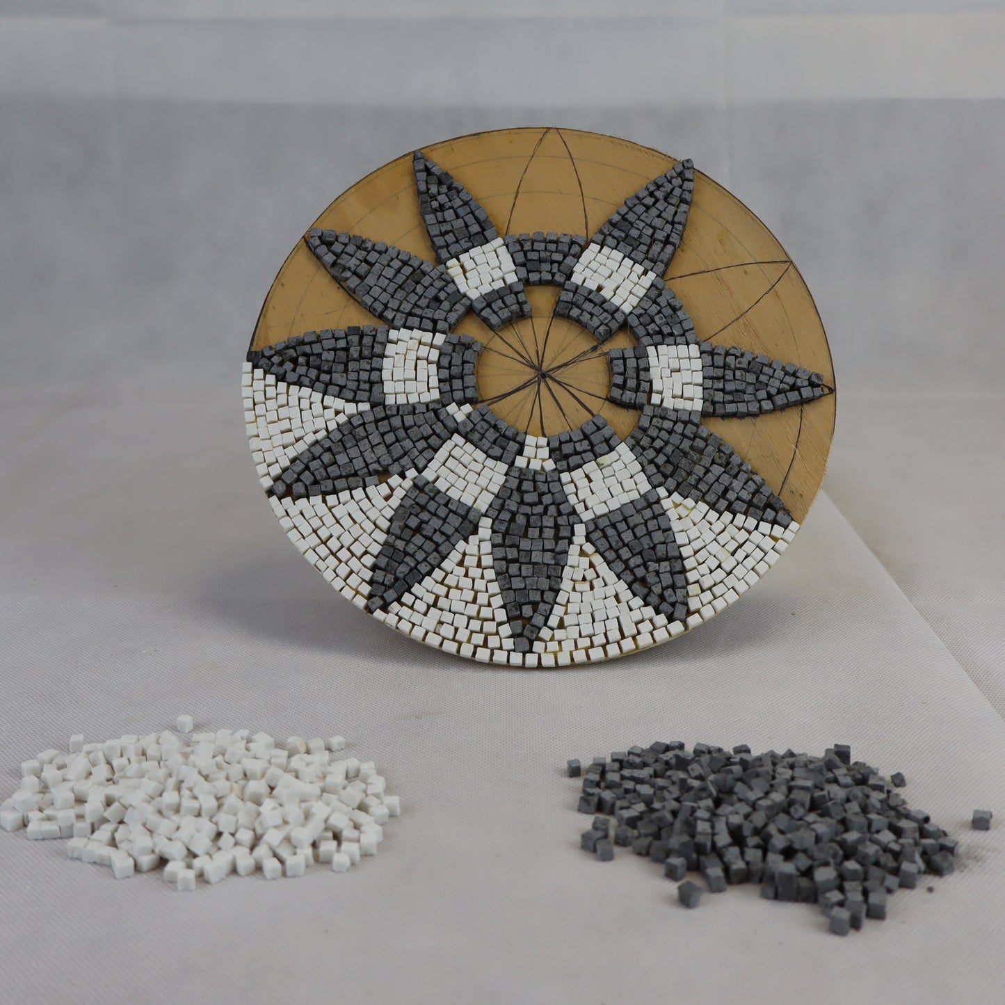 Rosone in costruzione su tavola di legno con sanpietrini di colore grigio scuro e bianco dimensioni 4x4 mm.