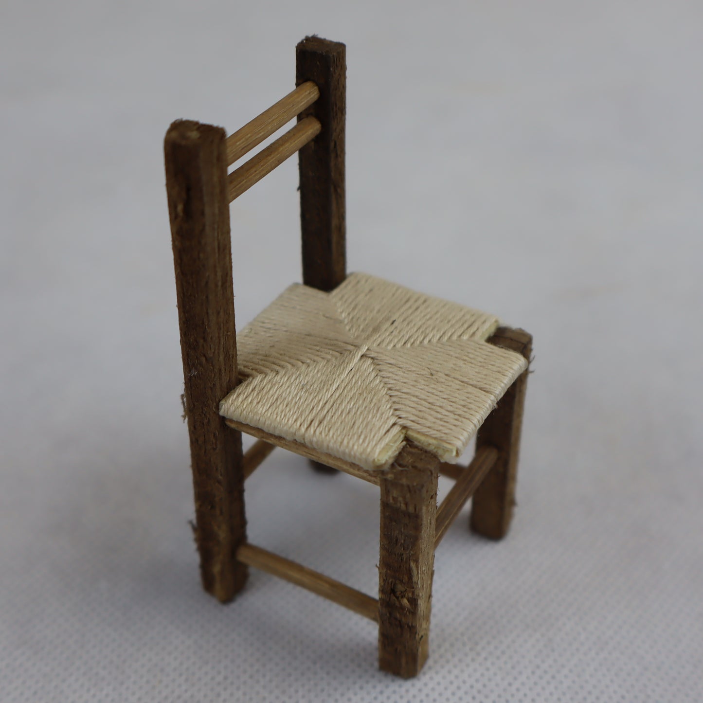 Miniatura artigianale di sedia rustica, realizzata in legno grezzo con seduta intrecciata in paglia naturale.
Le dimensioni contenute (8 cm di altezza x 4 cm di larghezza) la rendono ideale per ricreare ambientazioni rurali, scene contadine o interni tradizionali in presepi, diorami e plastici in scala ridotta.