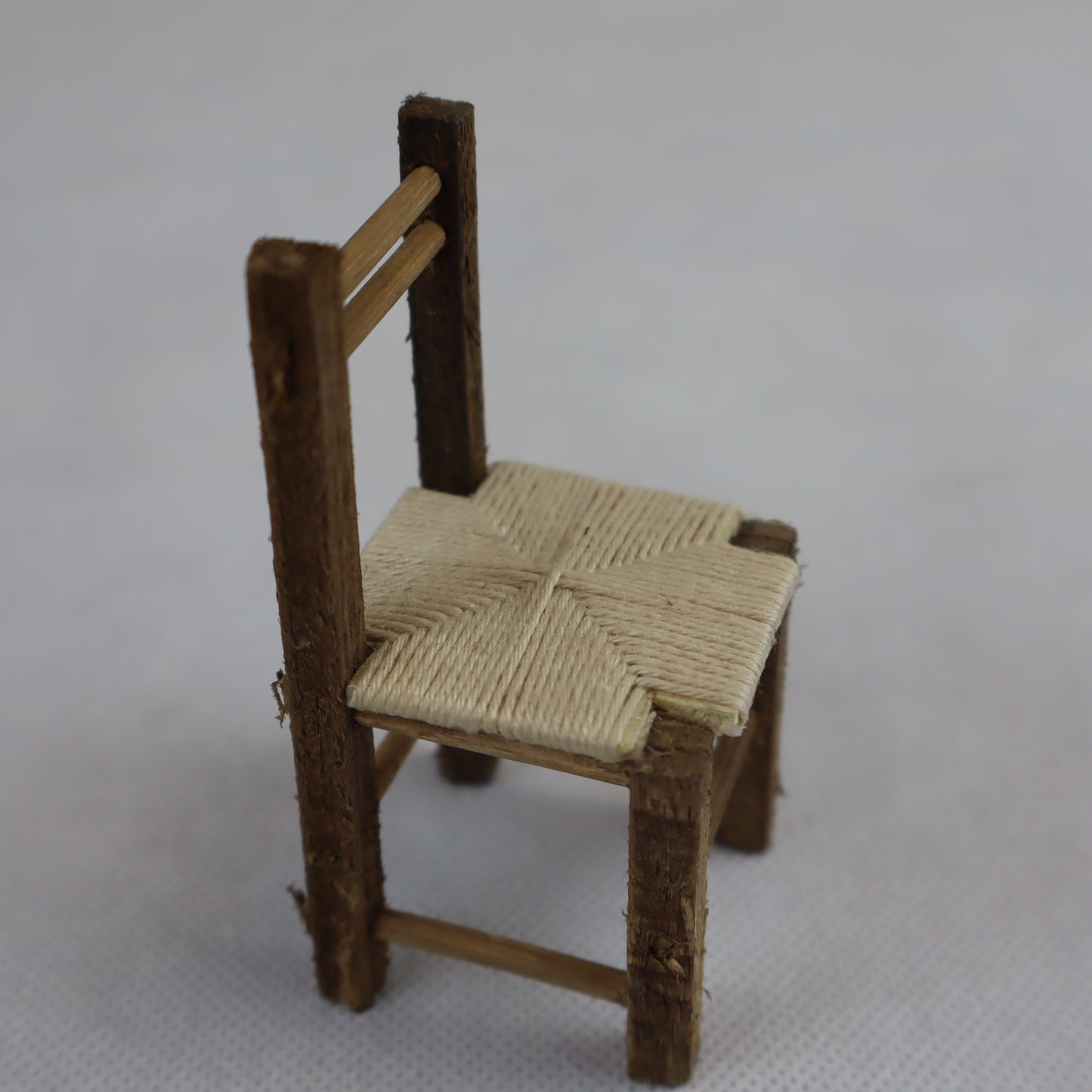 Miniatura artigianale di sedia rustica, realizzata in legno grezzo con seduta intrecciata in paglia naturale.
Le dimensioni contenute (8 cm di altezza x 4 cm di larghezza) la rendono ideale per ricreare ambientazioni rurali, scene contadine o interni tradizionali in presepi, diorami e plastici in scala ridotta.