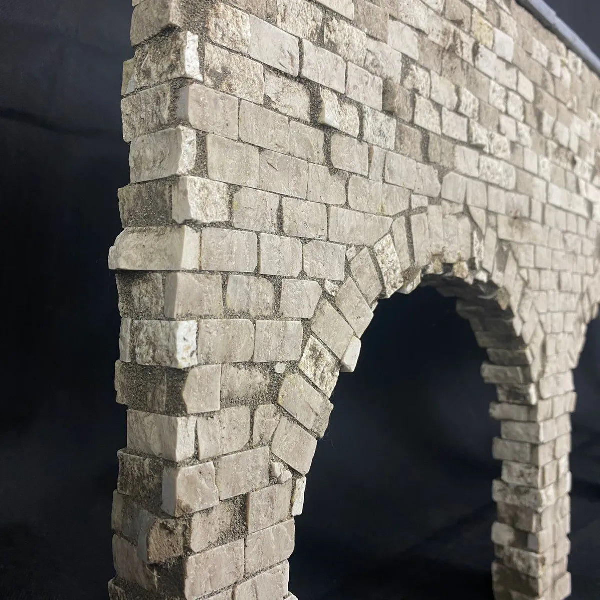 Vista laterale ravvicinata di una sezione di archi in pietra ricostruiti in scala, con texture realistica e finitura antichizzata, su sfondo nero.