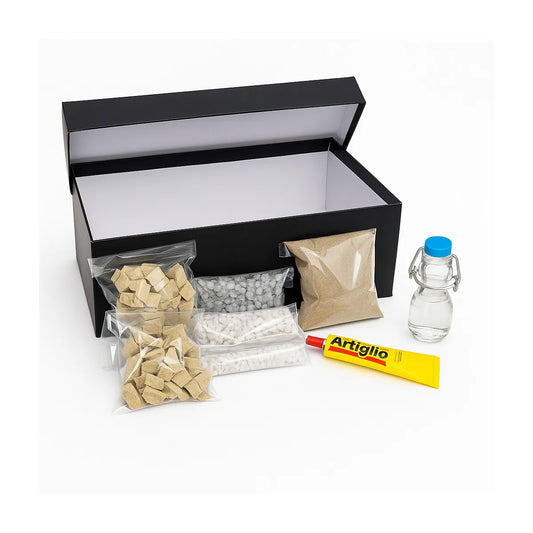 Kit “SpaccaNapoli” per mosaico artigianale, con scatola nera aperta e sacchetti di tessere in pietra beige, bianca e grigia, sabbia, colla Artiglio e bottiglia in vetro con tappo blu.
