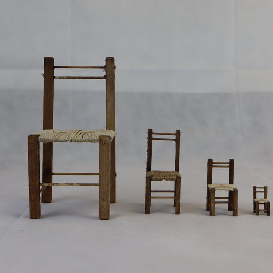 Quattro sedie rustiche in miniatura realizzate in legno grezzo, con seduta intrecciata in paglia naturale.
