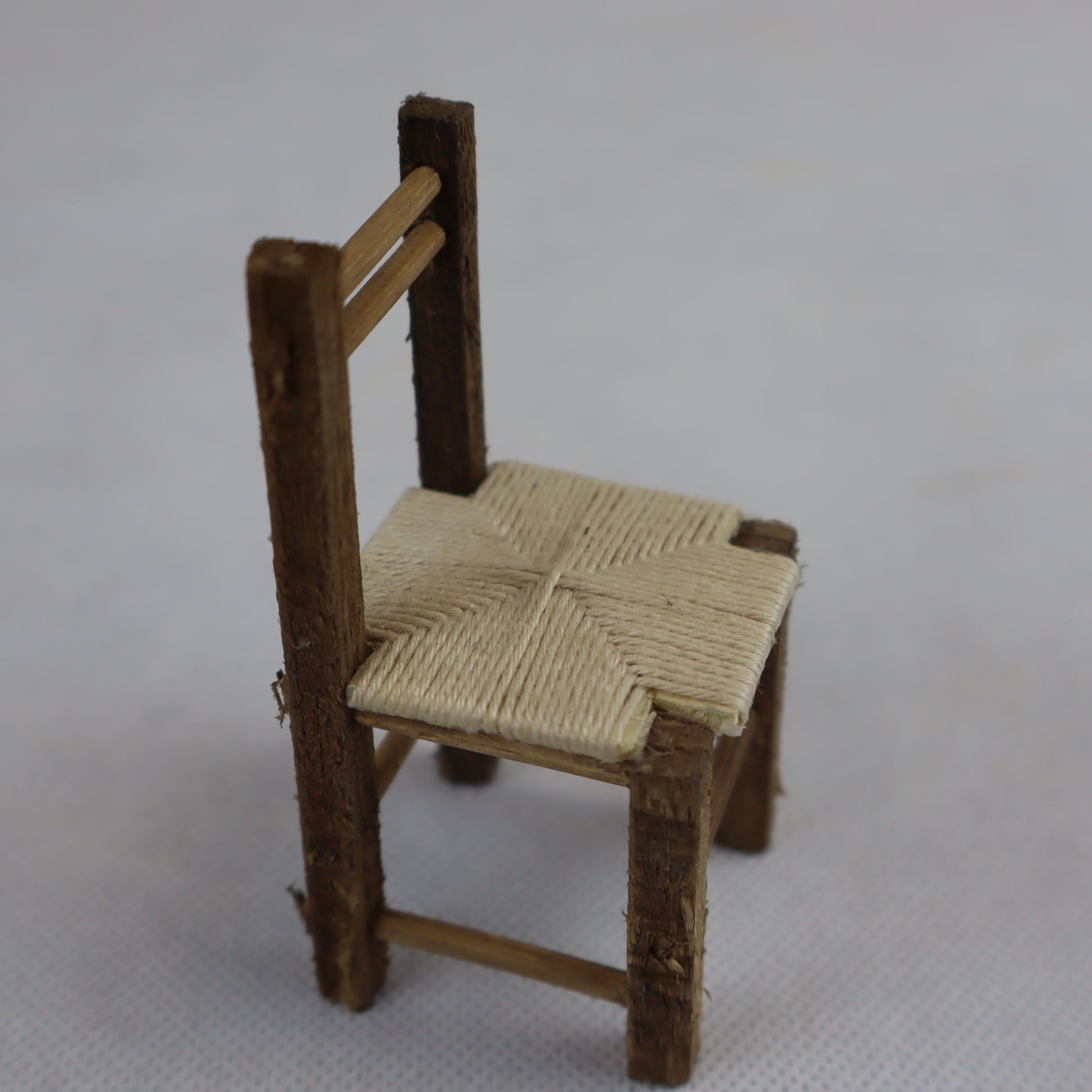 Miniatura artigianale di sedia rustica, realizzata in legno grezzo con seduta intrecciata in paglia naturale.
Le dimensioni contenute (8 cm di altezza x 4 cm di larghezza) la rendono ideale per ricreare ambientazioni rurali, scene contadine o interni tradizionali in presepi, diorami e plastici in scala ridotta.
