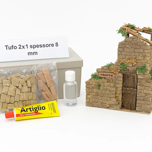 Kit per la costruzione artigianale di un rudere: struttura in miniatura in tufo, con vegetazione e insegna "Frutta", accompagnata da scatola grigia, sacchetti di mattoncini, flacone e colla Artiglio.