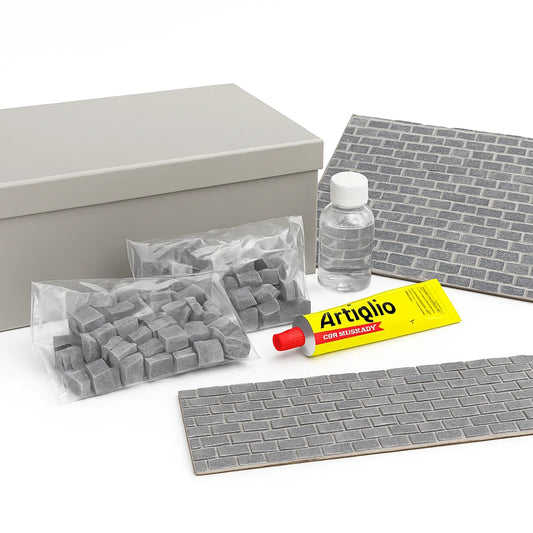 Kit "Costruisci la tua strada" esposto su fondo nero, con scatola grigia chiusa, sacchetti di cubetti in pietra grigia, tubetto di colla Artiglio e bottiglietta di liquido trasparente, accanto a una base stradale già assemblata.