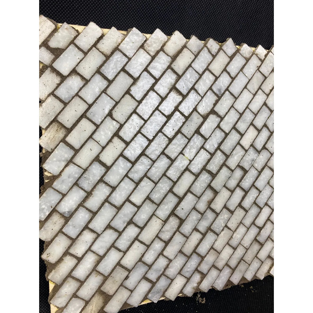 Mattonella in pietra naturale con mosaico rettangolare posato a spina di pesce su fondo scuro.
