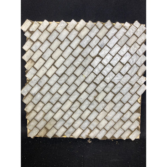Dettaglio ravvicinato di un mosaico in pietra bianca con fuga grigia su base inclinata, per presepi o miniature artigianali.