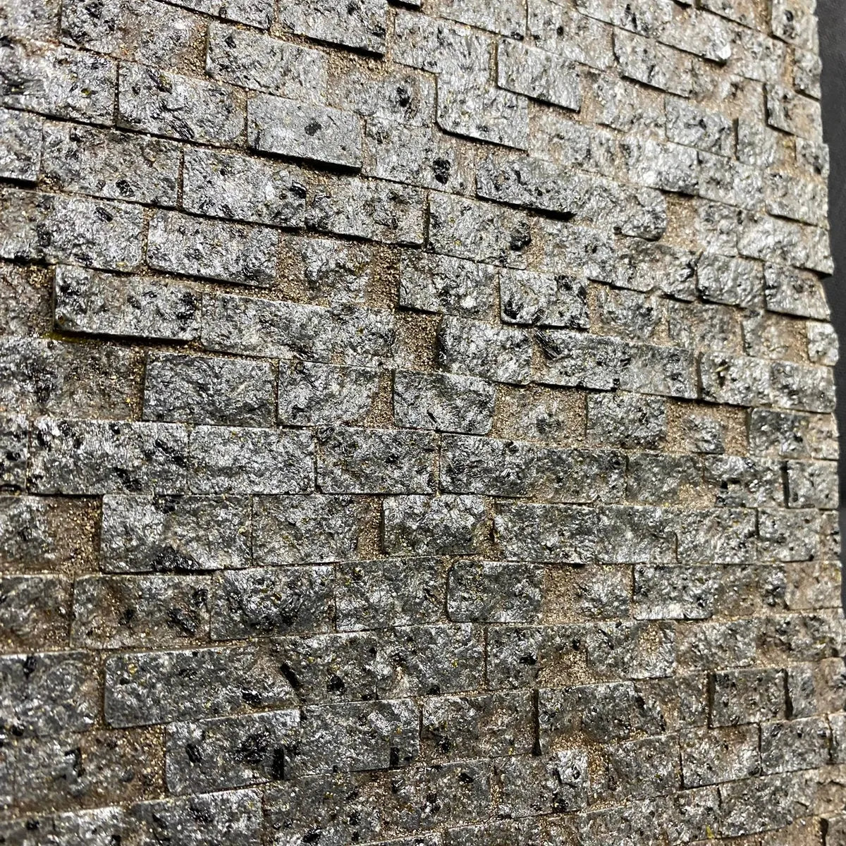 Parete in miniatura realizzata con pietre rettangolari grigie, effetto lucido e texture irregolare, ideale per ambientazioni rustiche o presepi artigianali.