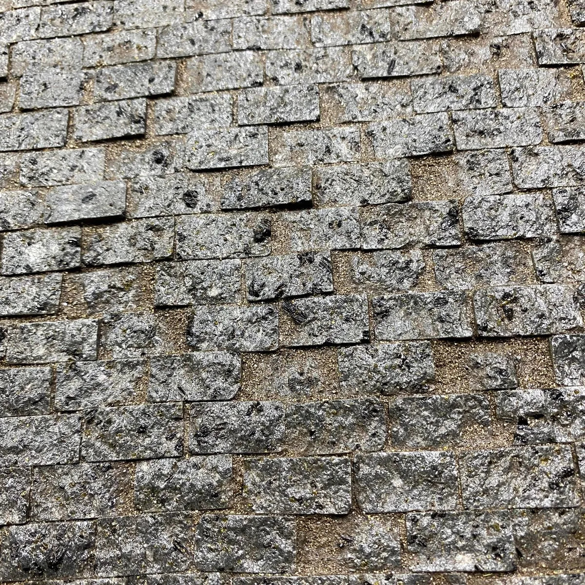 Dettaglio di rivestimento murario in miniatura con pietre scolpite e finitura opaca-granulosa, in tonalità grigio chiaro, per scenografie o costruzioni in scala.